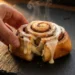 Overnight cinnamon rolls with heavy cream being pulled apart showing fluffy interior and cream cheese frosting